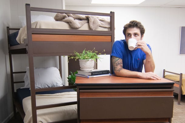 Man drinking coffee resting on chest of drawers