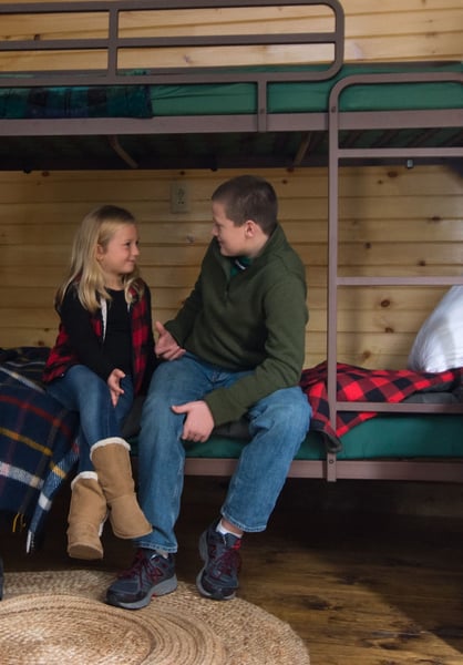 boy and girl sitting on a camp bunk bed talking and laughing 