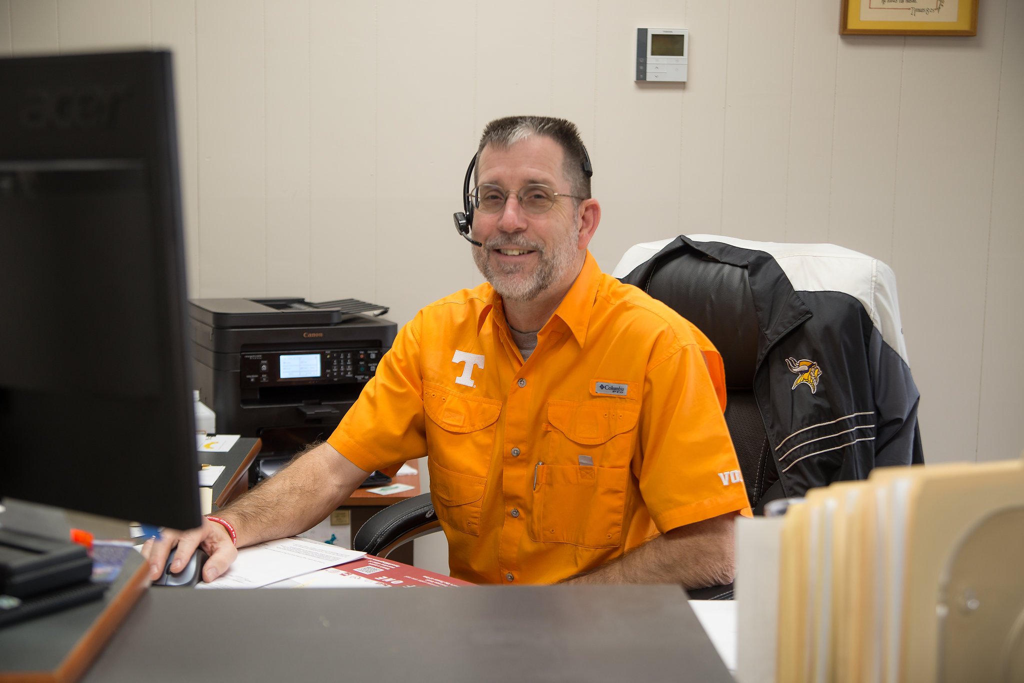 Man in orange smiling while sitting at computer